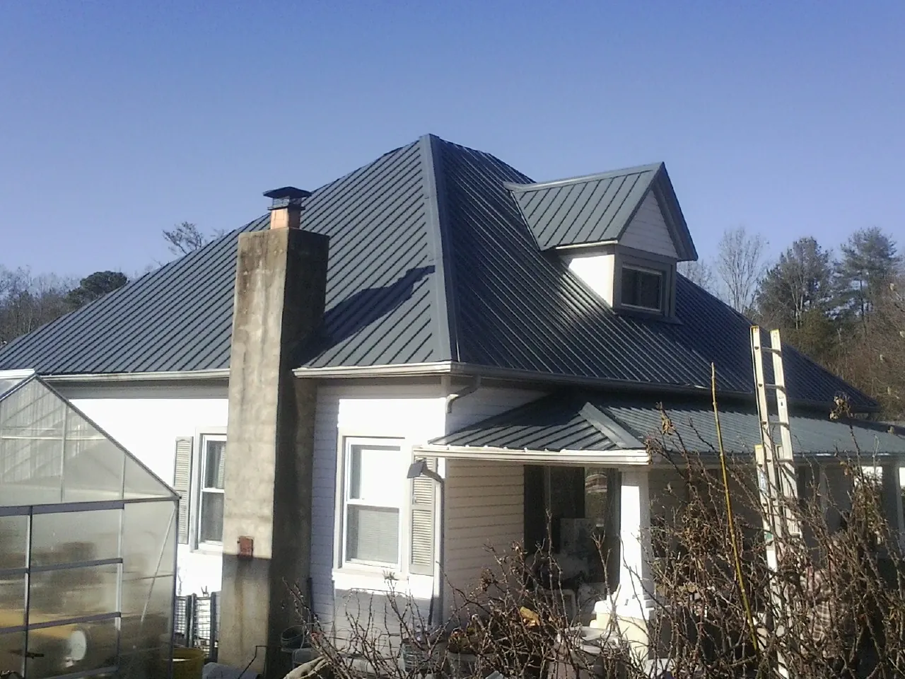 Dark blue standing seam metal roof on a white farmhouse with dormer — Slate & Tile Roof Repair by Roofing Brothers in Broomfield
