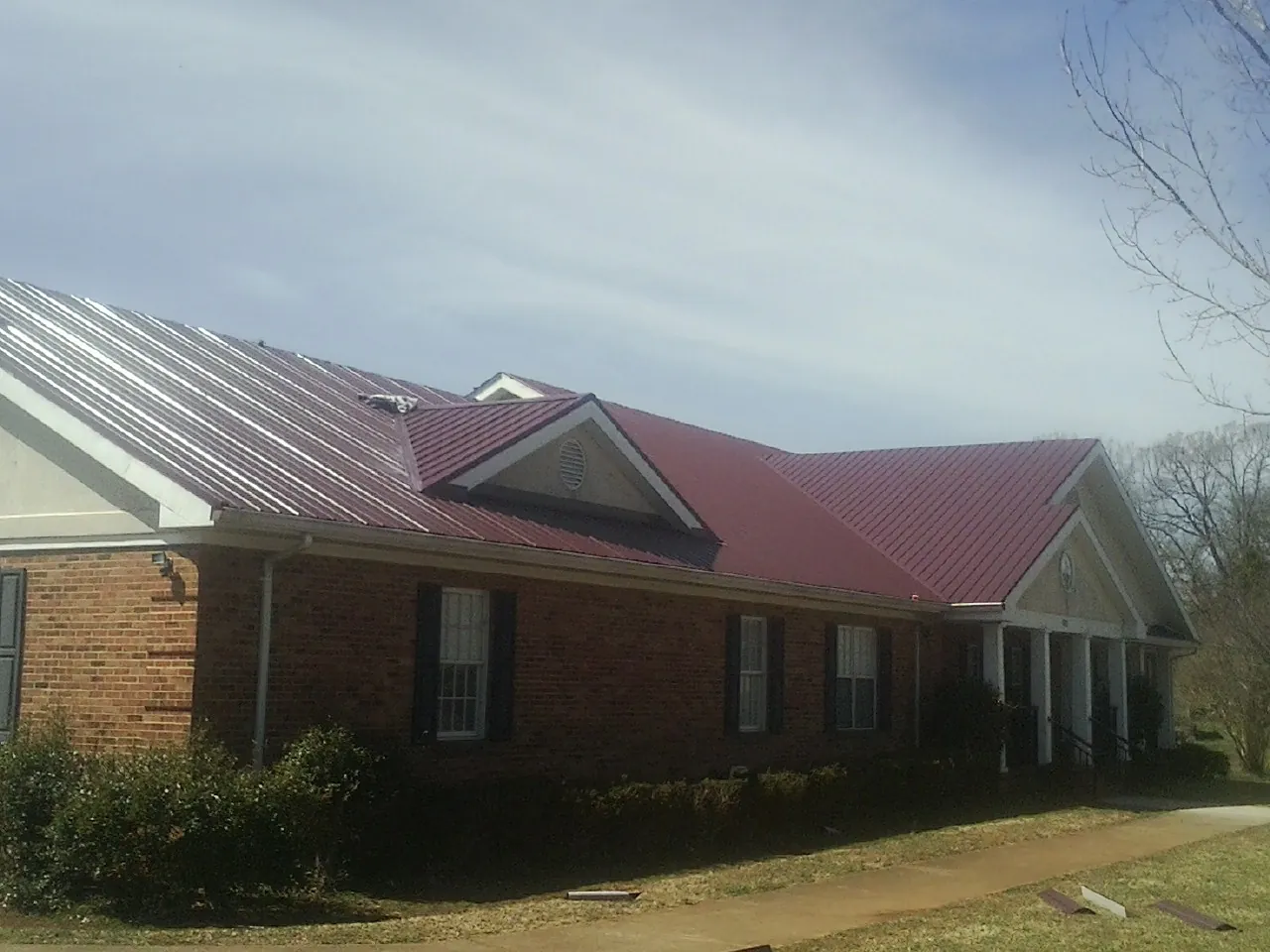 Red metal roof with gabled entries on a long brick building, from a Hail Damage Roof Repair job in Broomfield