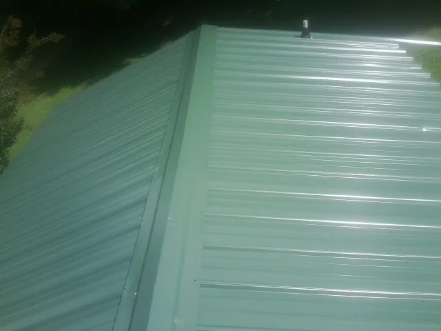 New green metal panels meeting at the ridge of a roof — Flat Roof Repair work by our crew in Broomfield
