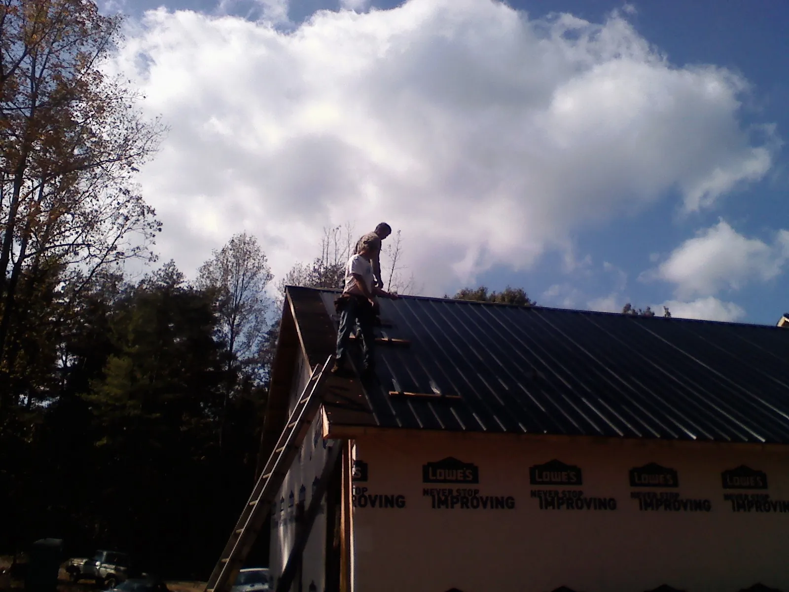 Roofer fastening dark metal panels high against a cloudy sky, from a Roof Inspection job in Broomfield