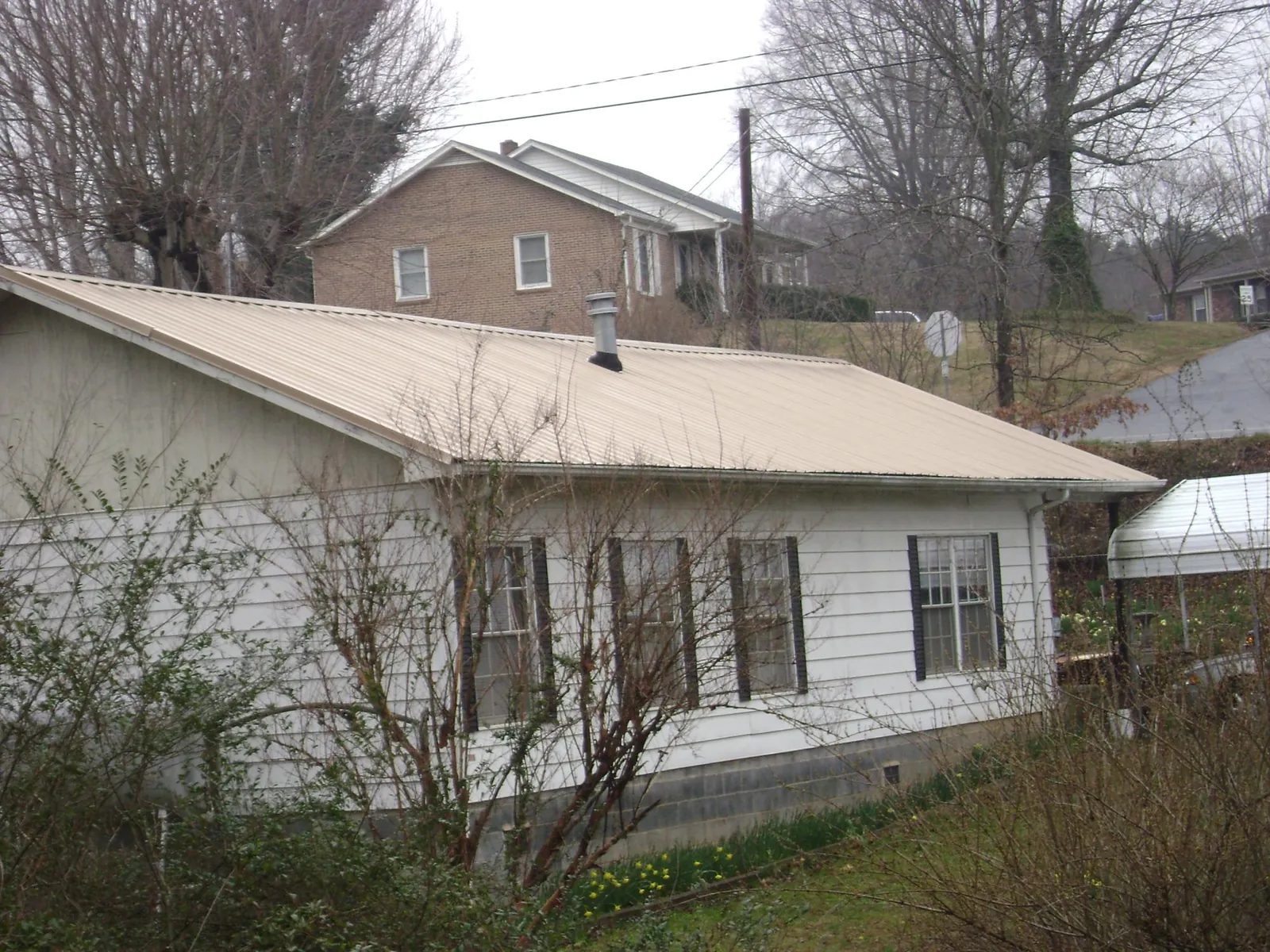 Tan metal roof on a white sided house set into a hillside — Commercial Roofing by Roofing Brothers in Broomfield