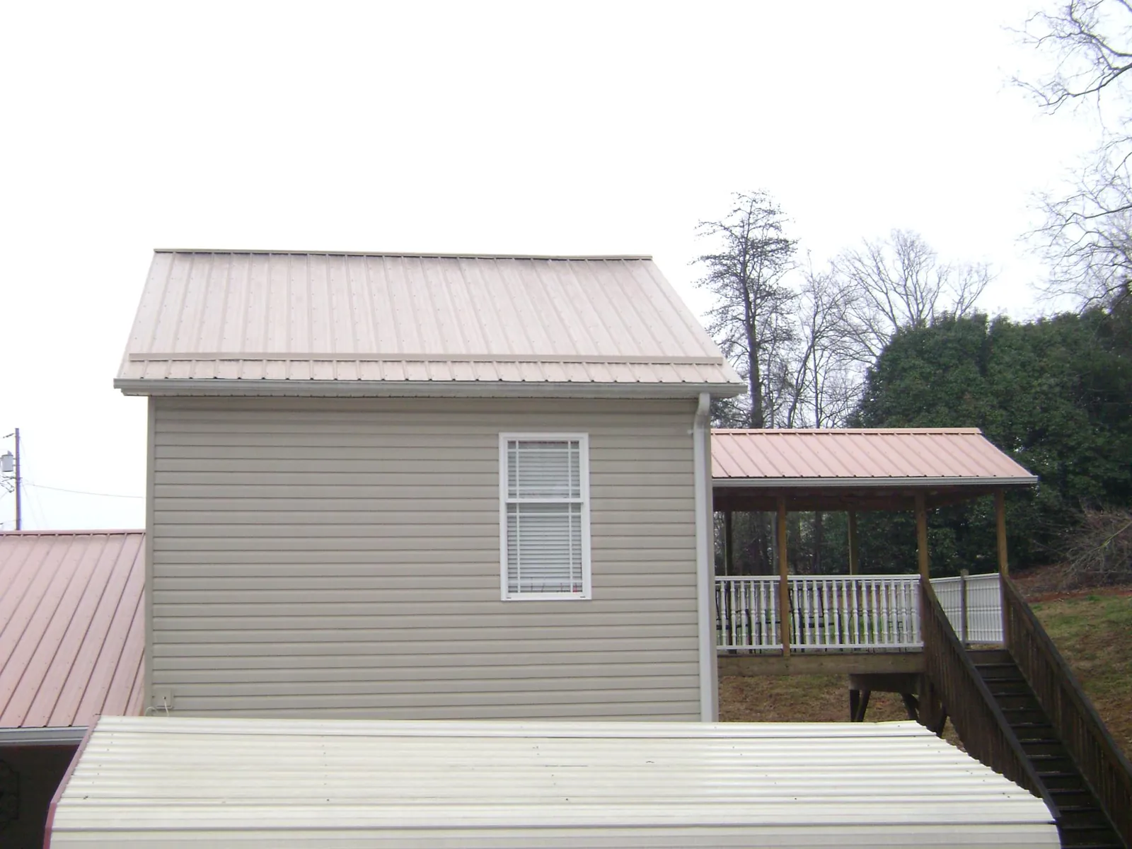 Tan metal roofs on a two story addition and attached porch, from a Roof Replacement job in Broomfield